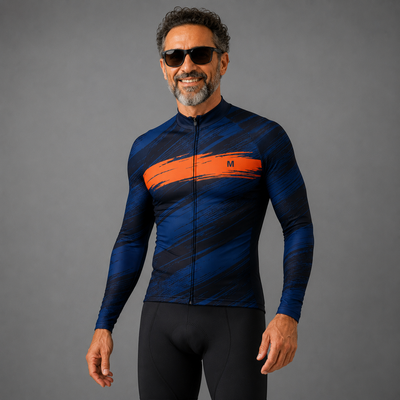 A man wearing a long-sleeve athletic cycling jersey with a blue and black abstract pattern and a bold orange chest stripe, paired with black cycling shorts, set against a solid gray studio background.