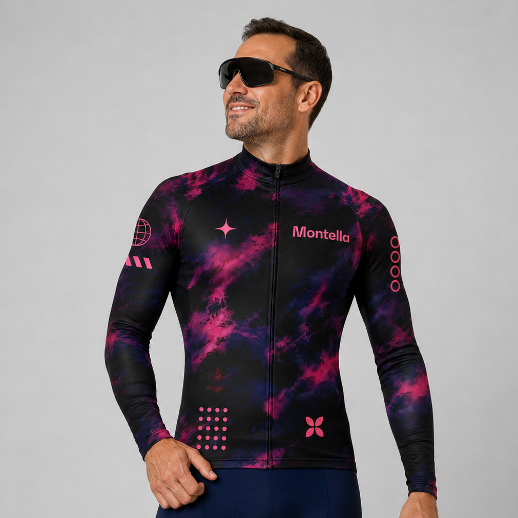 A man wearing a long-sleeve cycling jersey with a black and pink cosmic nebula pattern, paired with navy blue cycling shorts and black sunglasses, against a solid gray studio background.