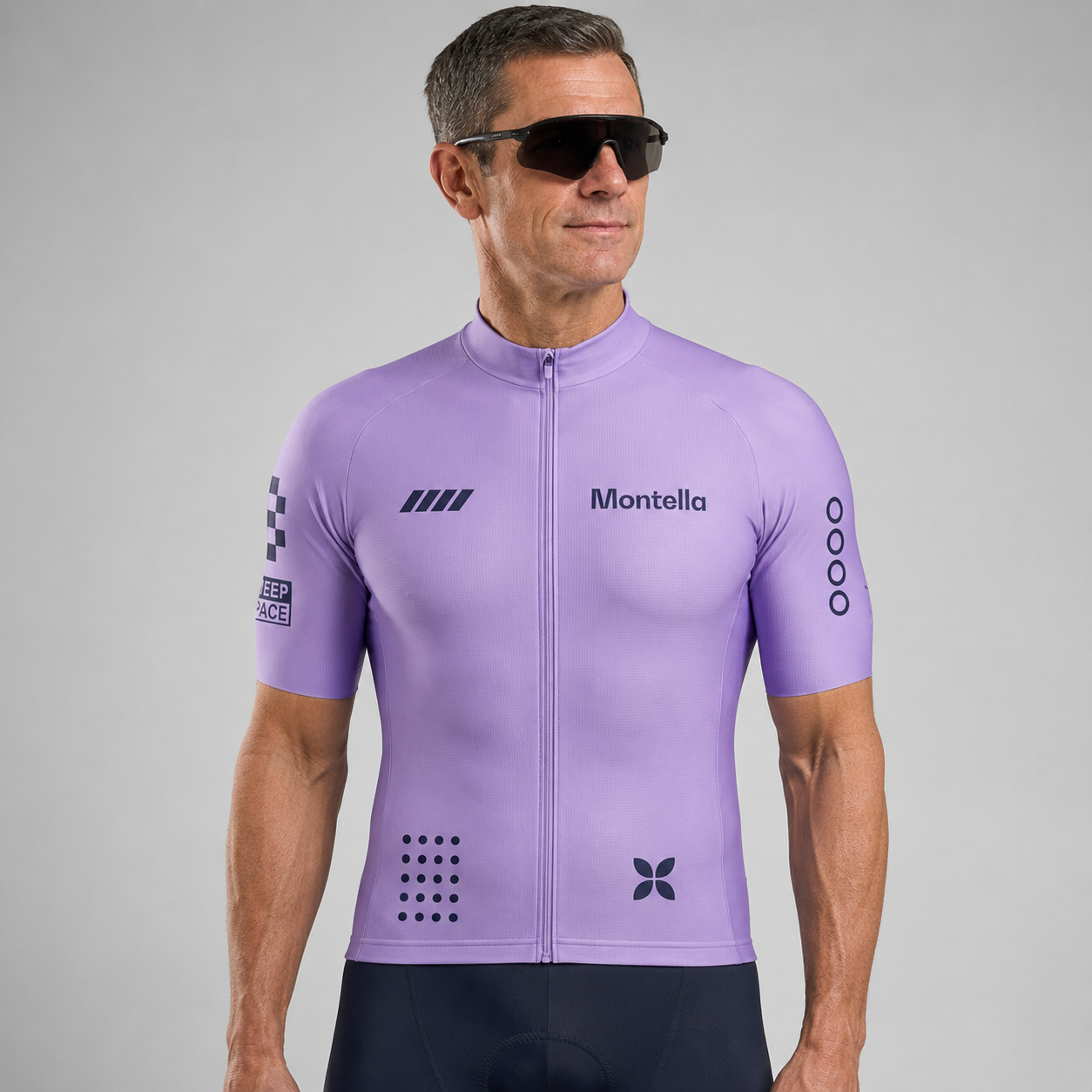 A man wearing a light purple Montella cycling jersey with black graphics and black cycling shorts, photographed against a neutral gray studio background.
