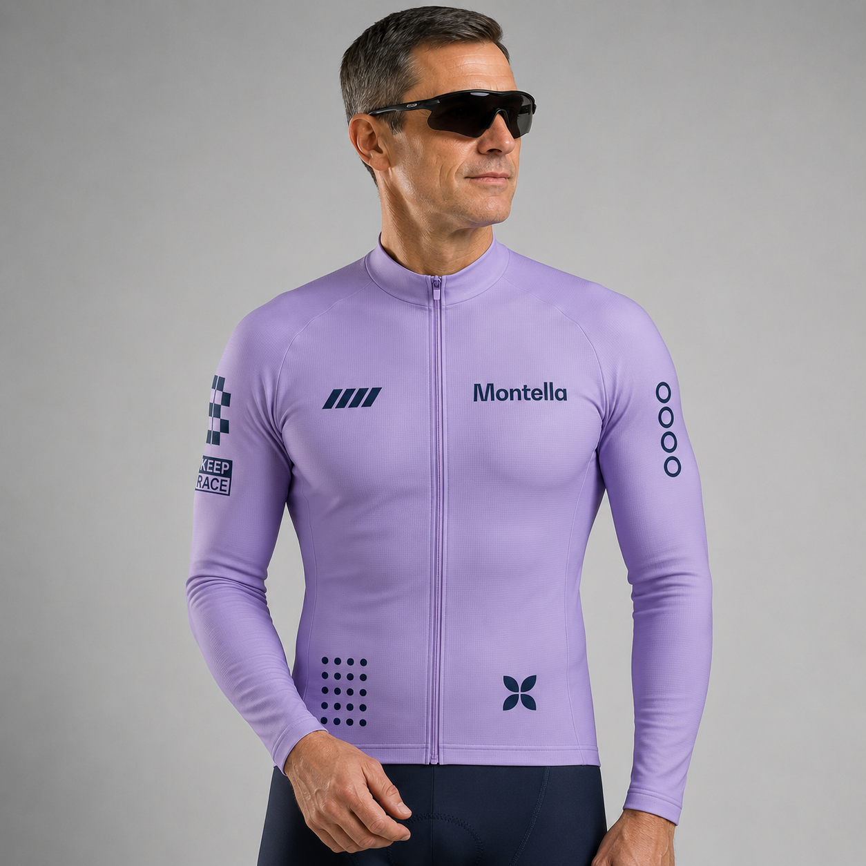 A man wearing a light purple long-sleeve cycling jersey with 'Montella' printed on the chest, black sunglasses, and dark cycling shorts, photographed against a neutral gray studio background.